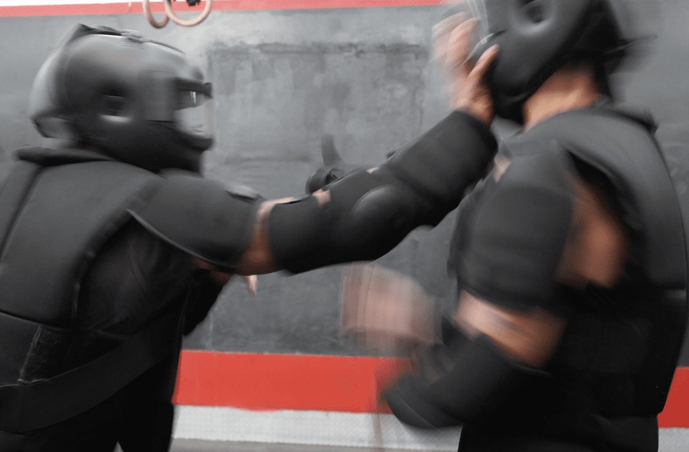 Two people in HIGH GEAR suits, one landing a palm strike